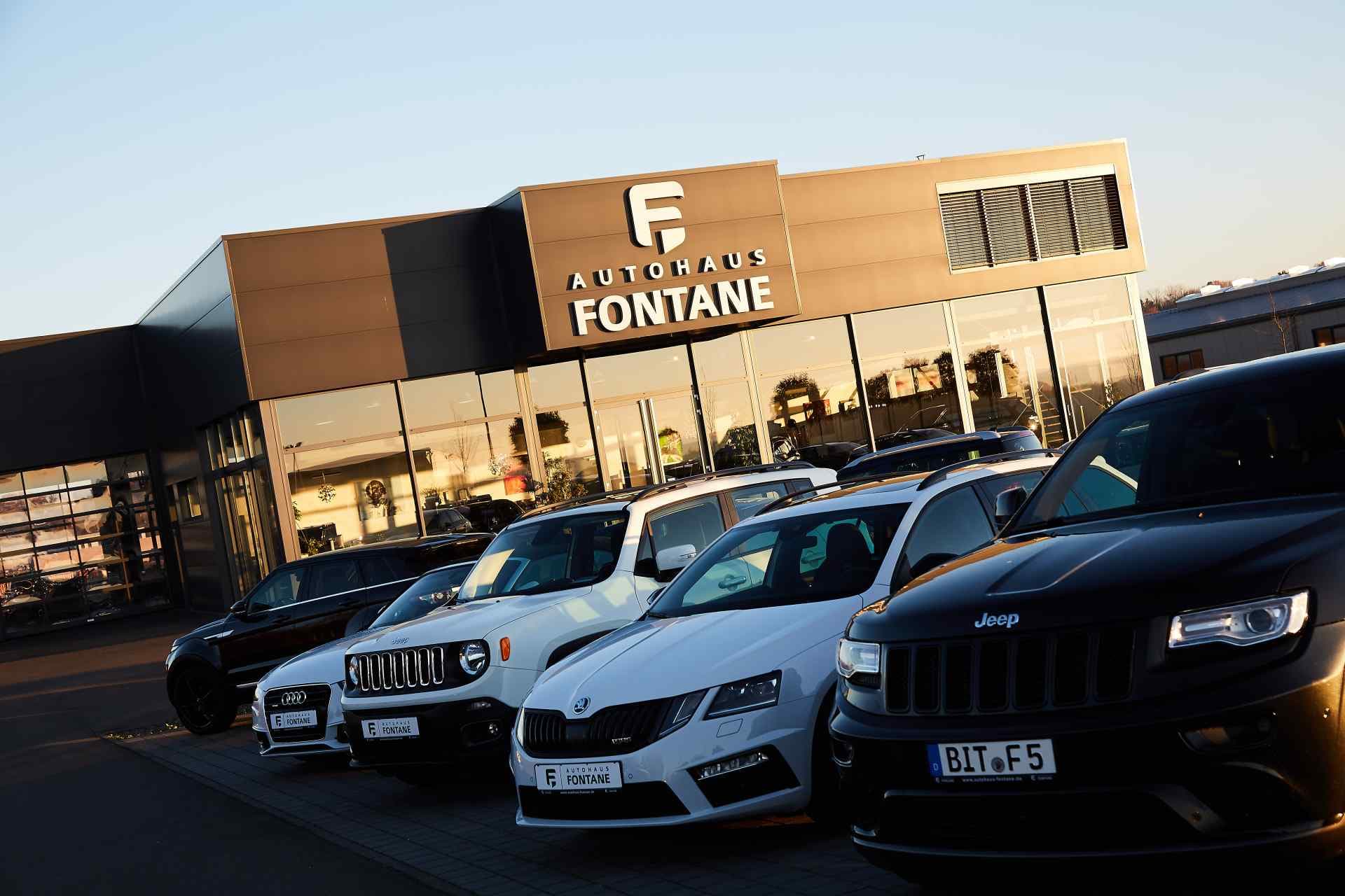 Das Autohaus Fontane im Abendlicht, davor die Fahrzeugreihe